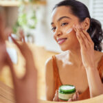 A woman applying skincare products in front of a mirror