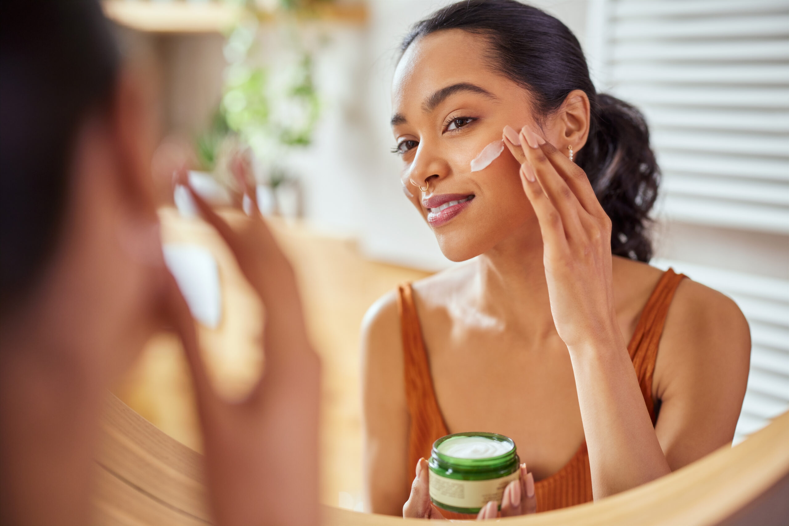 A woman applying skincare products in front of a mirror